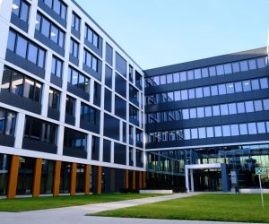 Modern office building with large glass windows and a courtyard lawn in front.